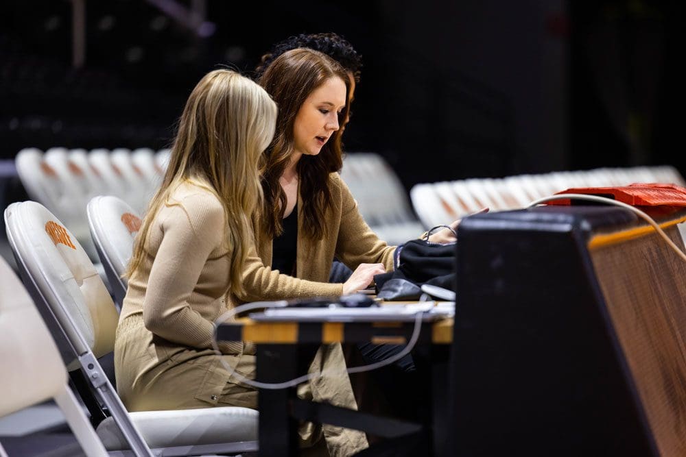 Alumnus Courtney Lyle sits at a table court side with a student who is shadowing her.