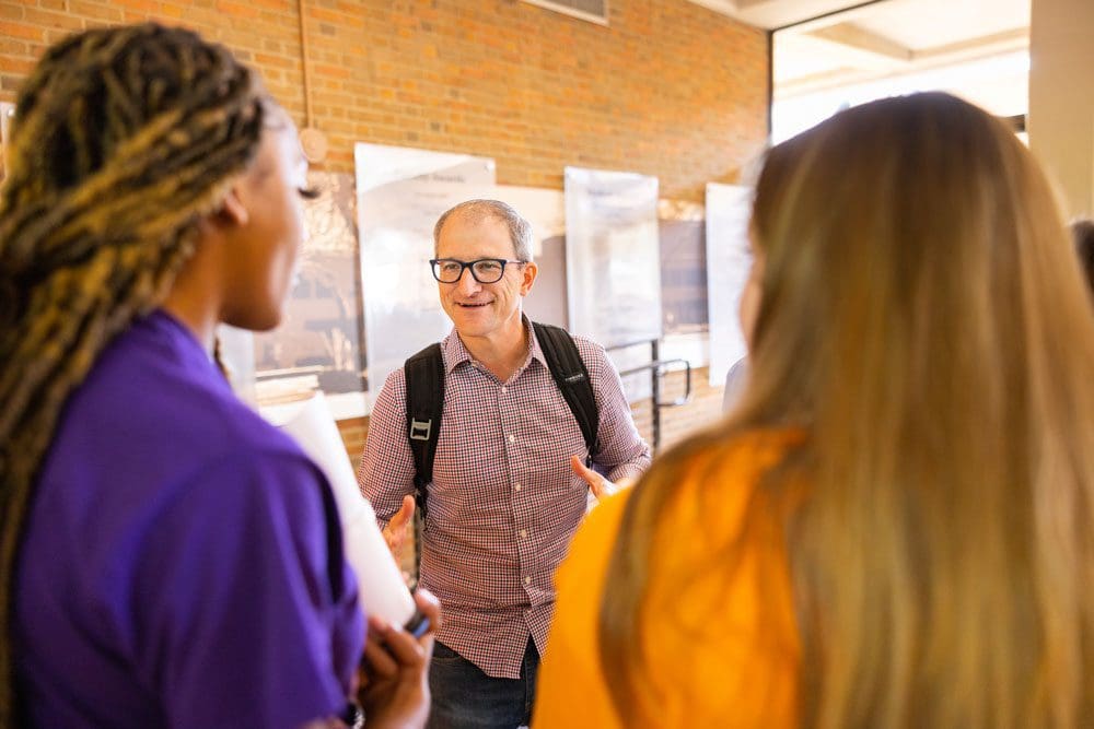 Associate Professor Nick Geidner smiles and talks to two students.