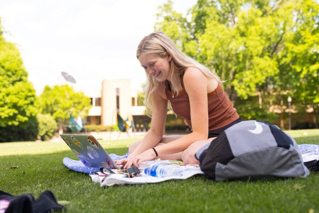 A student sits in Circle Park's grass and works on a laptop.