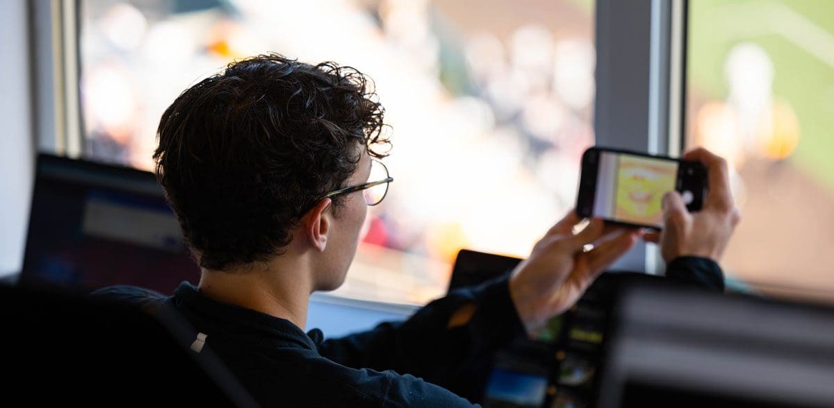 A student uses their phone to take a photo of a football game.