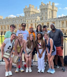 A group of students pose in front of a castle in the United Kingdom, with JEM Professor Guy Harrison