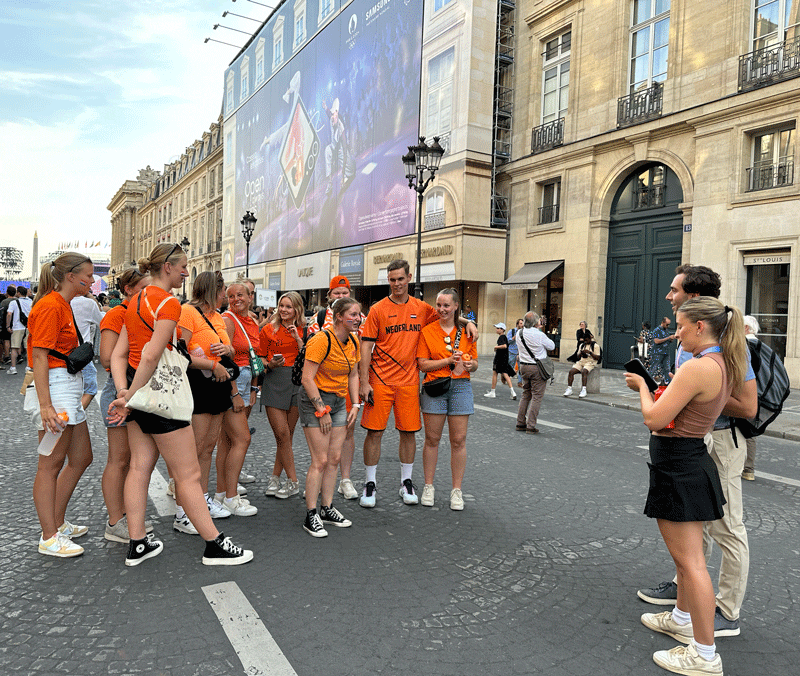 Students Lillian Van Alsburg and Griffin Hadley interview a group of several Netherlands fans clad in orange shirts.